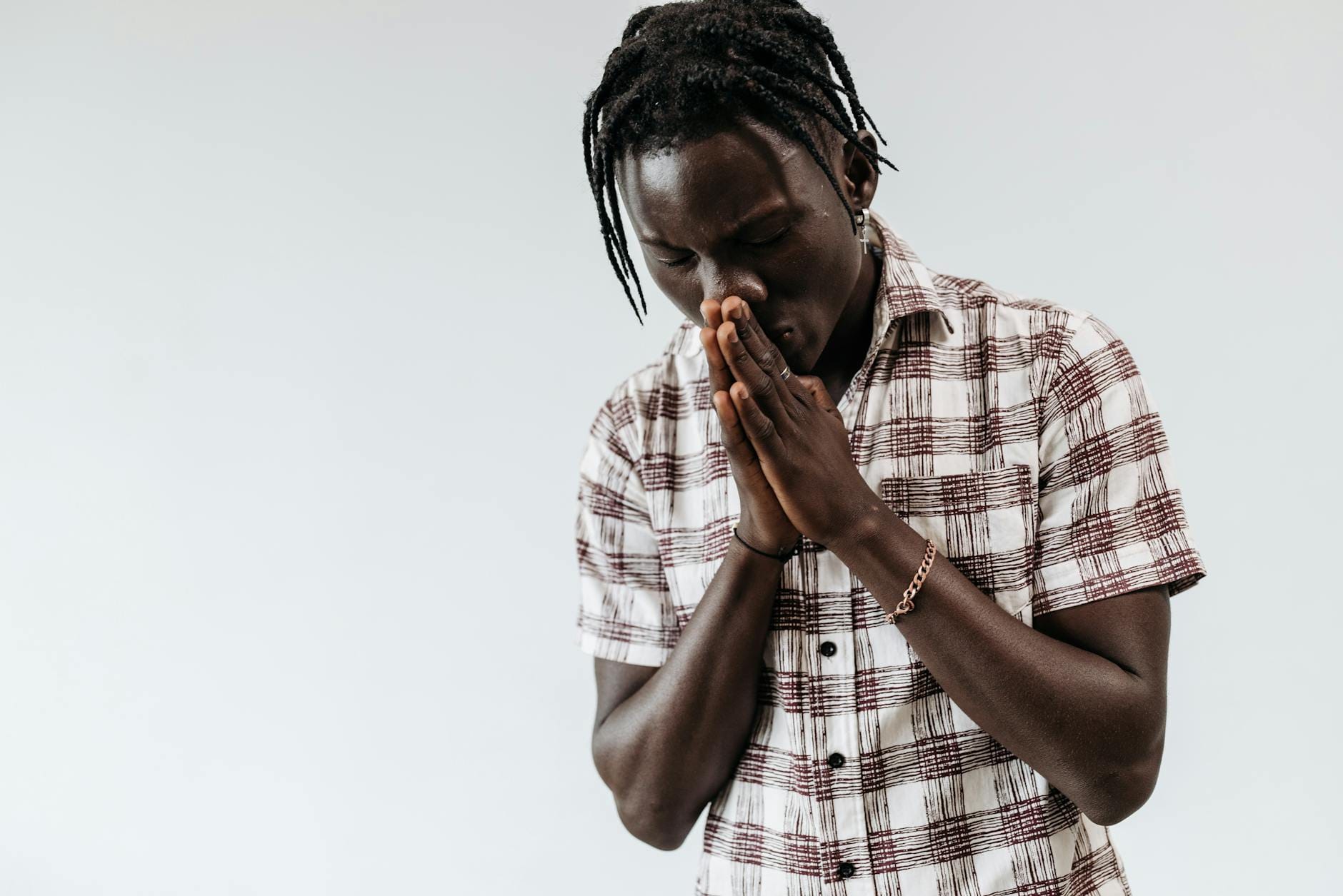 Młody mężczyzna w koszuli w kratę modli się, składając dłonie