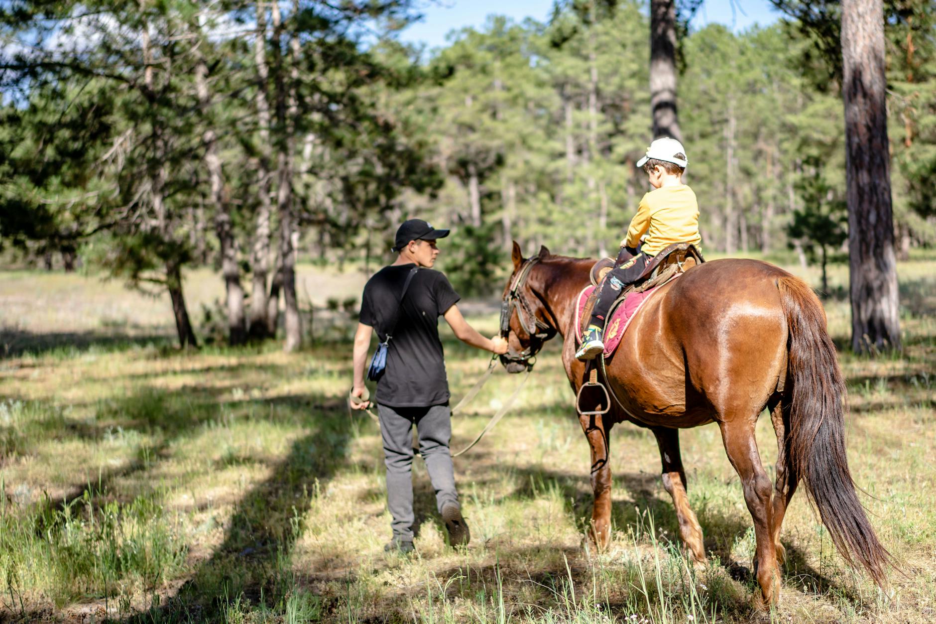 Jak zorganizować weekend w siodle: plan dnia, przerwy i regeneracja po jeździe Instruktor prowadzi dziecko na koniu leśną ścieżką podczas słonecznego dnia