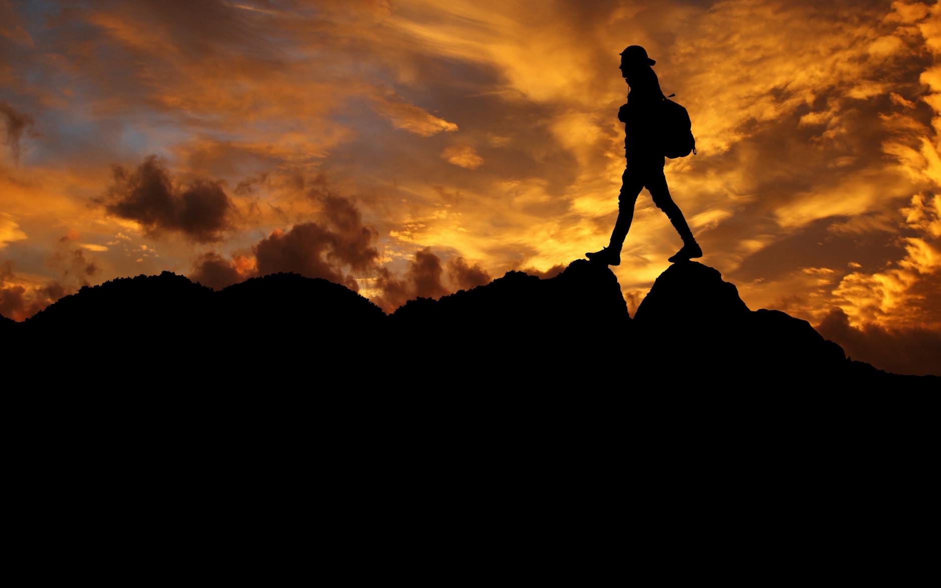 Sylwetka turysty z plecakiem na górskiej grani o zachodzie słońca