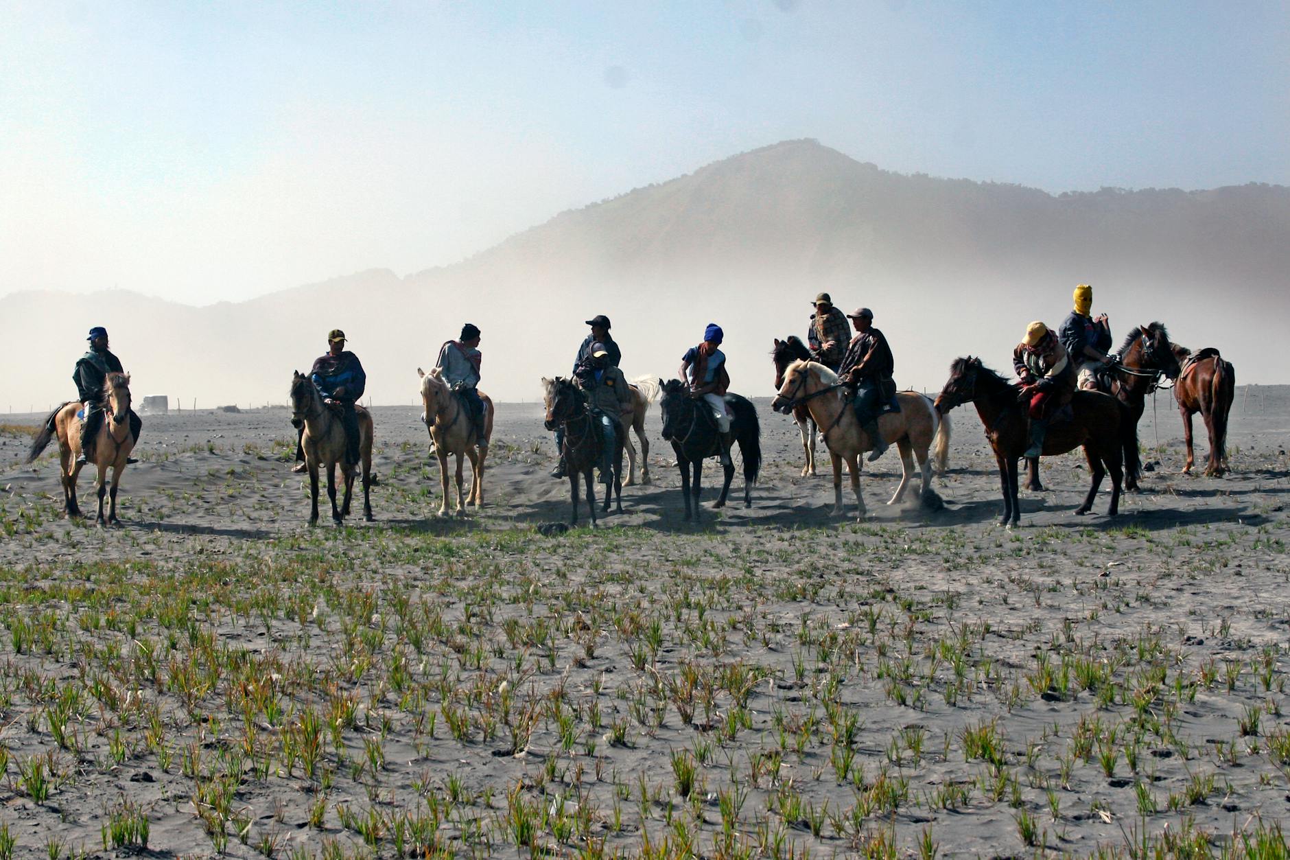 Grupa jeźdźców jedzie konno po mglistym polu na tle gór