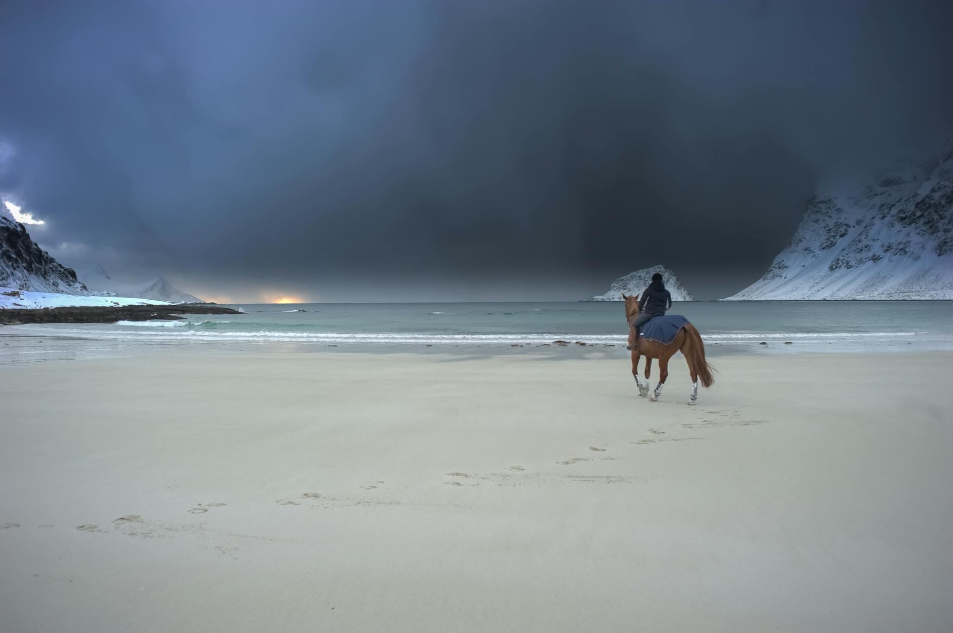 Jeździec na koniu galopuje po mglistej plaży pod burzowym niebem
