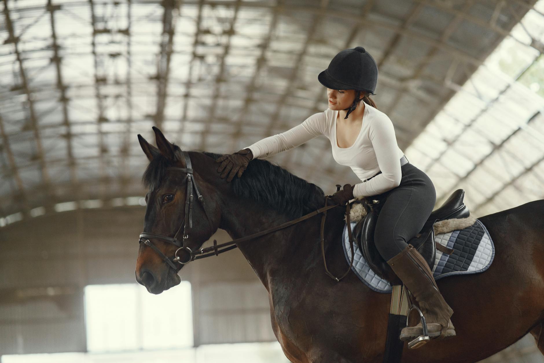 Kobieta w kasku jeździeckim podczas jazdy konnej w krytej hali