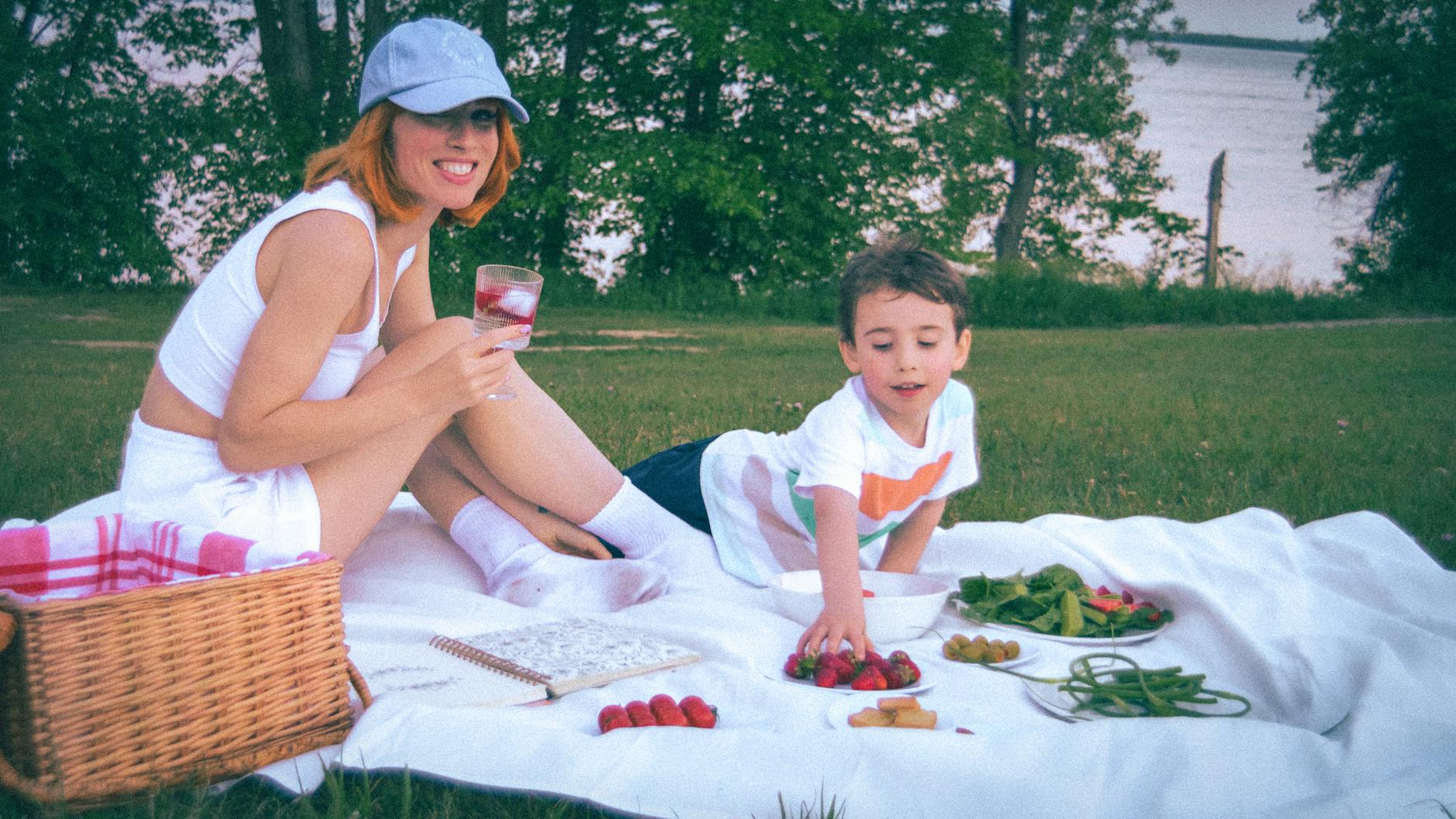 Mama i dziecko jedzą owoce na kocu podczas letniego pikniku nad stawem